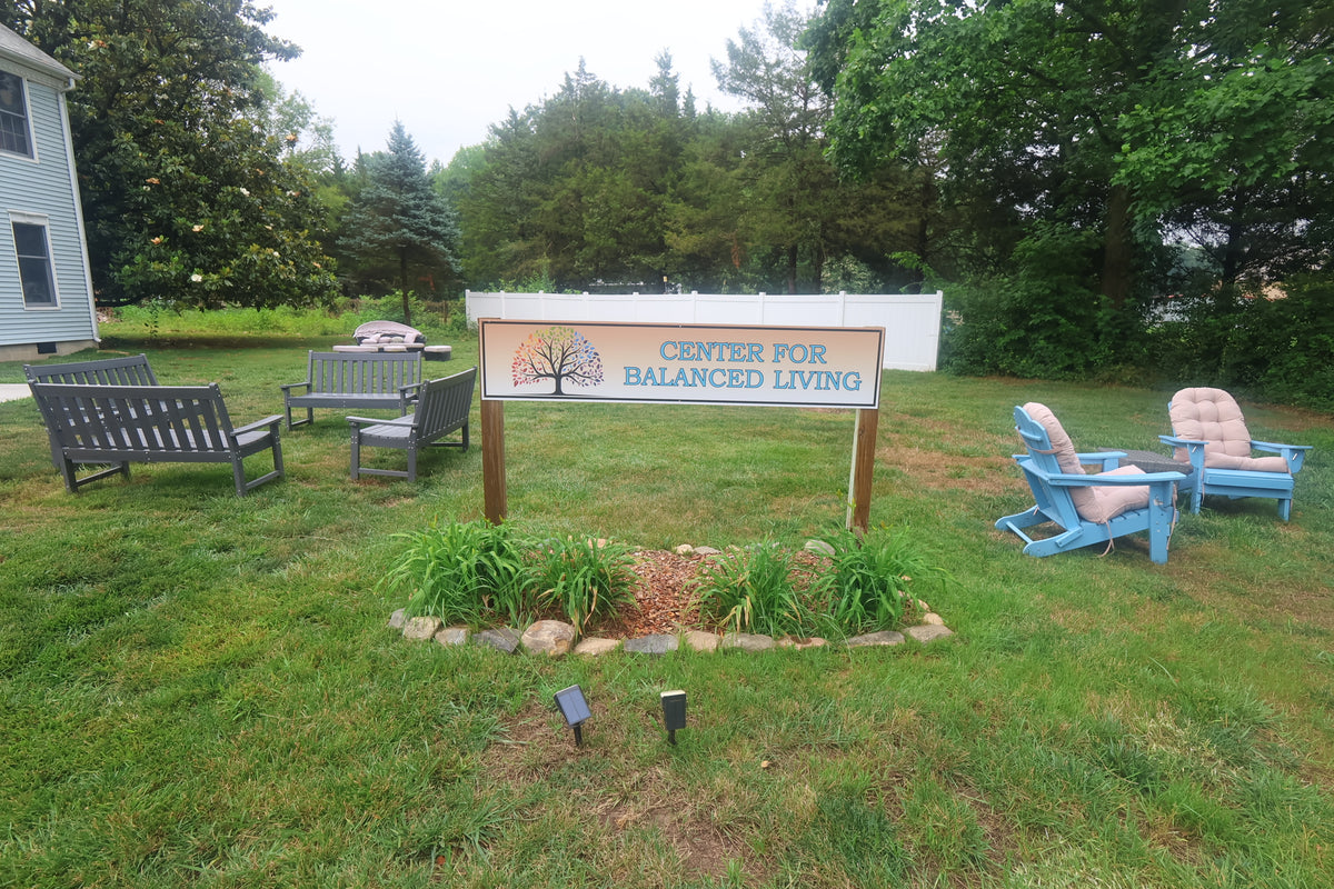 Center for Balanced Living sign with the rainbow tree logo, outdoor benches and blue Adirondack chairs on the lawn beside the Townsend office