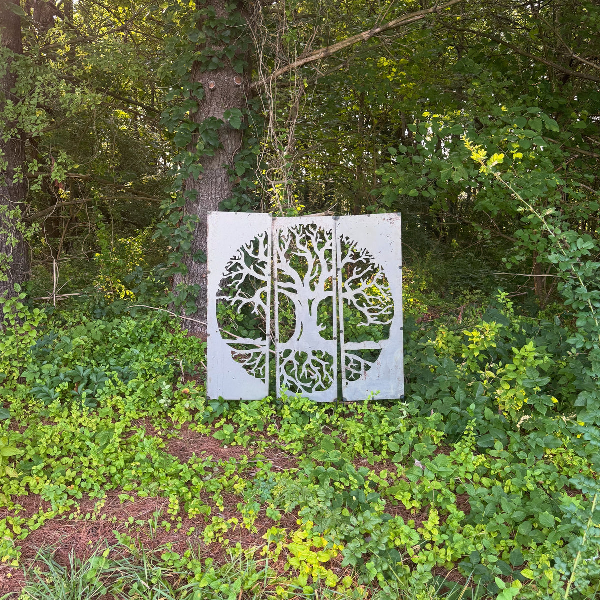 Metal tree of life sculpture set among trees and ground cover on the Center for Balanced Living property