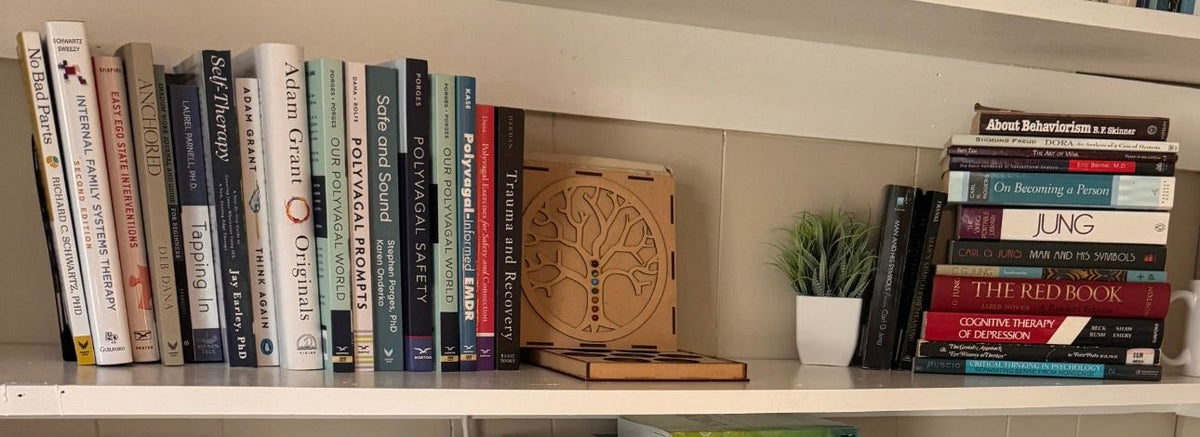 Dr. Niki Serravalle's office bookshelf: Internal Family Systems, polyvagal and EMDR texts beside a stack of Jung, Rogers and Freud
