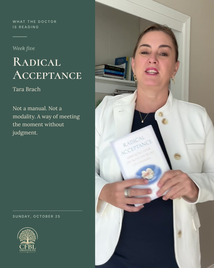 Dr. Niki Serravalle smiling, holding Radical Acceptance by Tara Brach beside her bookshelf. What the Doctor Is Reading, week five, Sunday October 25.