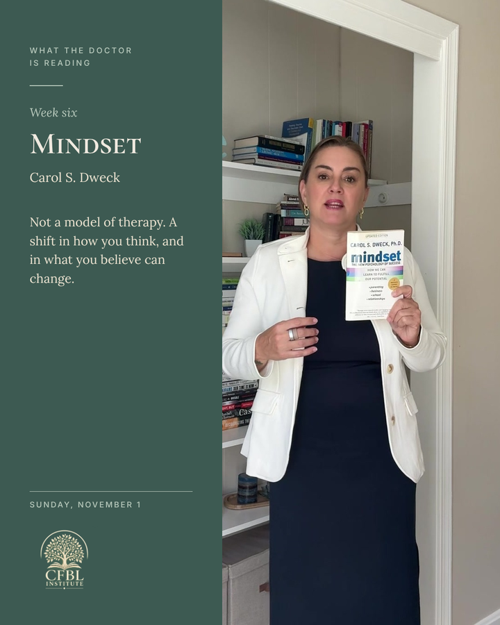Dr. Niki Serravalle holding Mindset by Carol S. Dweck beside her bookshelf. What the Doctor Is Reading, week six, Sunday November 1.